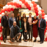 A group of 10 people stand beneath a balloon arch.