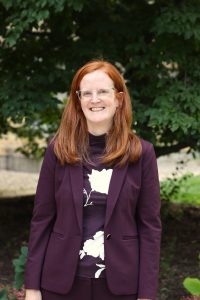 Emily Cauble, a middle-aged woman with fair skin, red hair, and blue eyes.