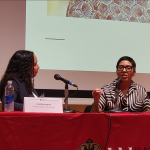 Two women of color speaking at a table.