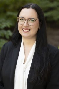 Photo of Bridget Lavender, a young woman with fair skin, long black hair, and brown glasses.