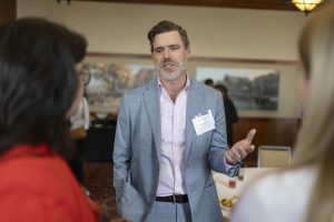 A man in a light gray suit chats with two women.