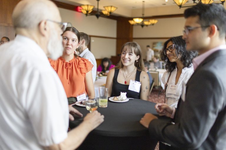 Three women speak with two men at a table.