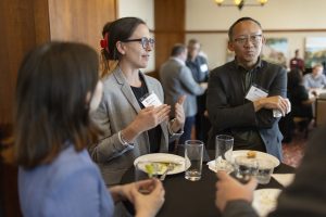 Several people stand around a table with dishes and glasses nearby.
