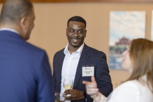 A black man in a suit smiles while holding a glass of champagne.