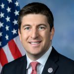 Photo of middle aged man beside a flag.
