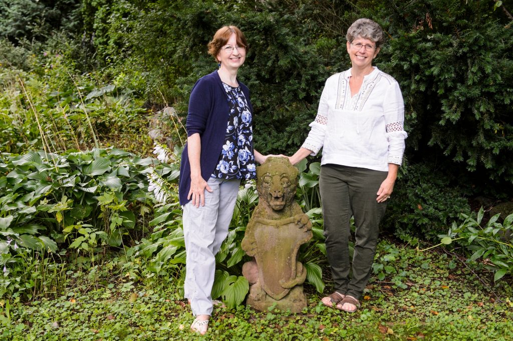 Sisters Joanna Rice and Jennifer Bakke standing with the garoyle in their parents garden