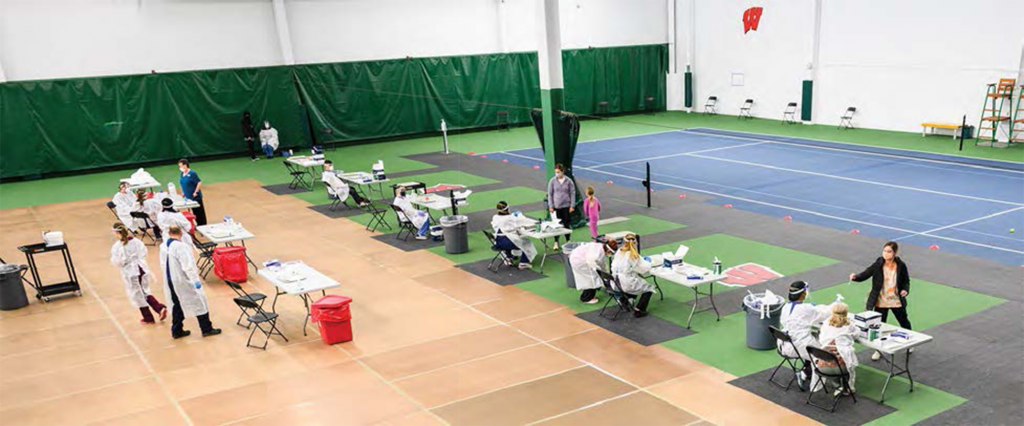 Photo of largely empty gymnasium with tables and a few students testing at them.