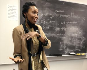 Gredaian Diplomat Dessima Williams presenting in front of a blackboard