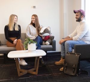 Three people smiling and sitting around a coffee table.