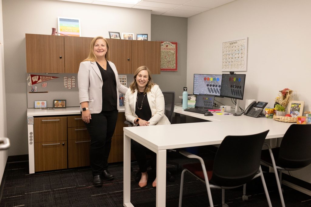 Two women stand together in an office.