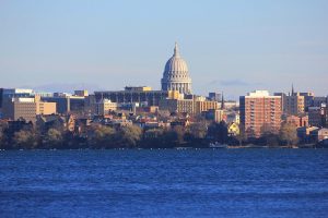 The capitol building of Madison, Wisconsin stands above the skyline along the lake shore.