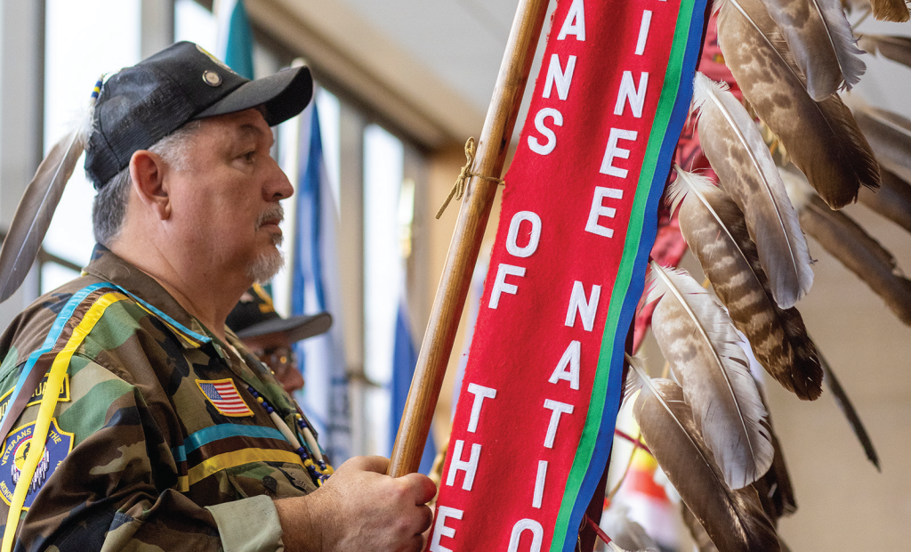 A person wearing a hat while holding a flag with feathers attached.