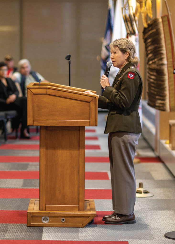 Person speaking into a microphone at a podium in front of a crowd.