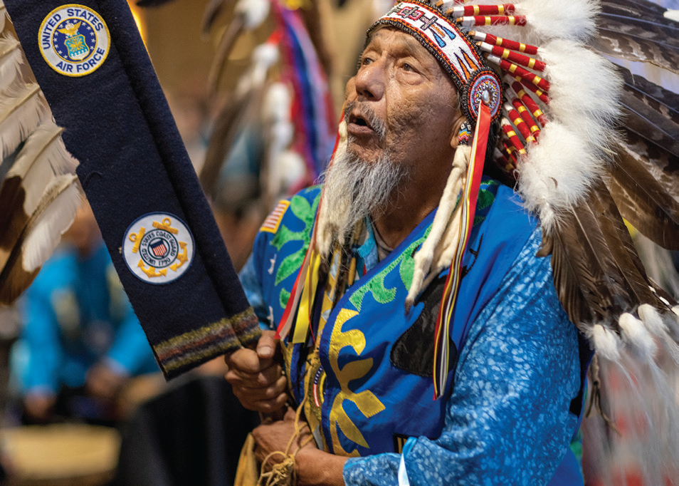 A person wearing feathered head attire while holding a flag with feathers attached.