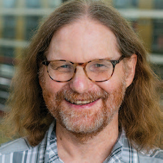 A headshot image of Jay Tucker, smiling and wearing glasses