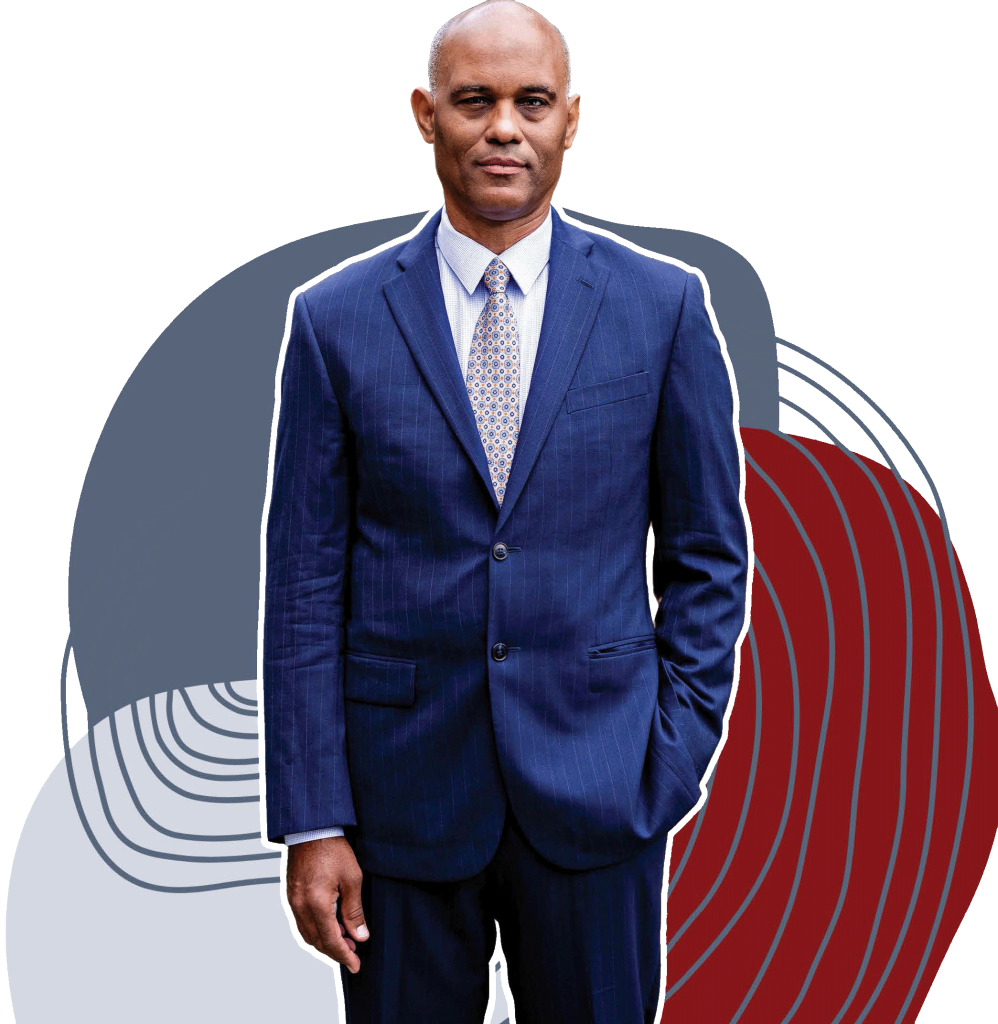 A photo of Thomas W. Mitchell, a black man wearing a navy blue suit, finely patterned dress shirt, and a red, blue and white patterned tie. He looks at the camera with a serious expression and stands in front of abstract illustrations.