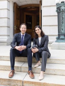 A man and a woman in business attire sit together on stone steps. They are Robert Yablon and Miriam Seifter, Co-Directors of the State Democracy Research Institute.
