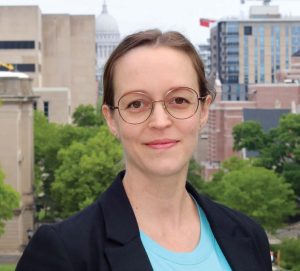 A photo of Nina Varsava smiling in front of a city skyline with trees nearby.