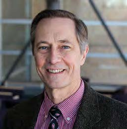 Headshot photo of John Ohnesorge, smiling at the camera and wearing a dark charcoal suit jacket over a plum shirt with a patterned dark tie.