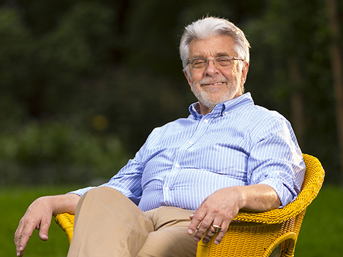 Photo of Ralph Cagle sitting back in a lawn chair in front of grassy area with trees.