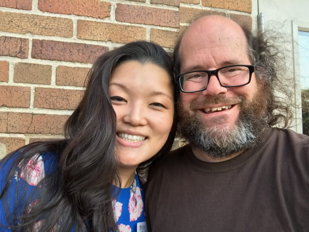 Michelle Yun smiling alongside Mike Hall while standing outside a brick building.