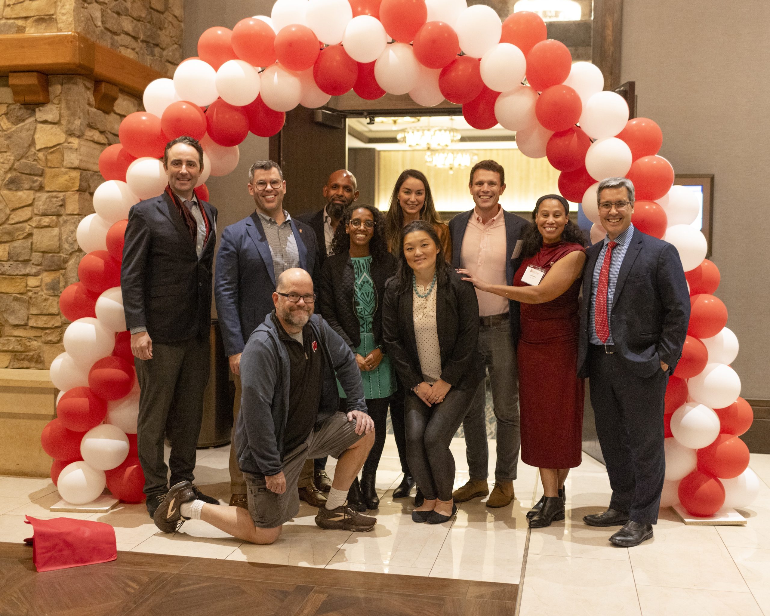 A group of the graduates smile in a group photo in front of a balloon arch alongside Dean Dan Tokaji.