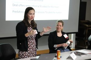 Presenters speaking at a table with a screen behind them.