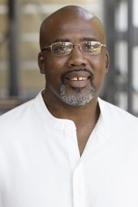 Headshot photo of Dant'e Cottingham, a black man with a shaved head, wireframe glasses, and a graying goatee.