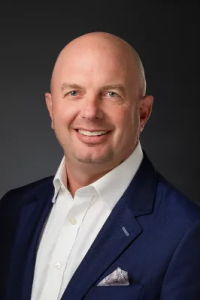 Photo of Jeff Kowieski, a man with a bald head and wearing a blue suit with white shirt and smiling.