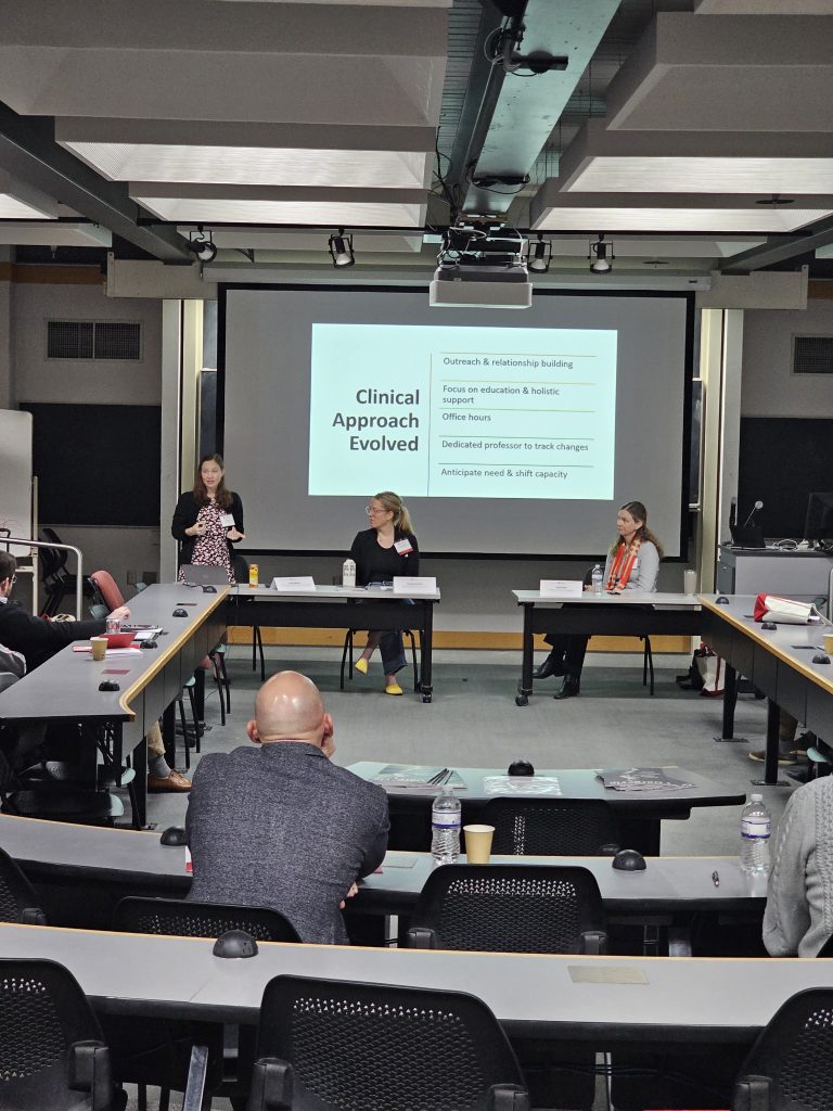 Photo of Wilson, Buchholz, and Patel seated before a crowd with a screen behind.