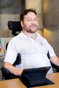 Photo of Mike Mohr in his powered chair at a desk.