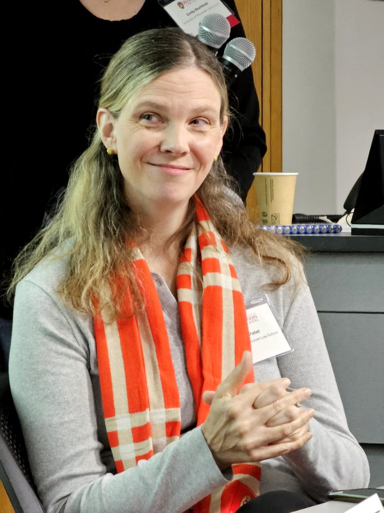 Photo of Tami Patel clapping while smiling and wearing a gray long sleeve top and an orange scarf.