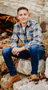 A young man in flannel and jeans sits on a rock.