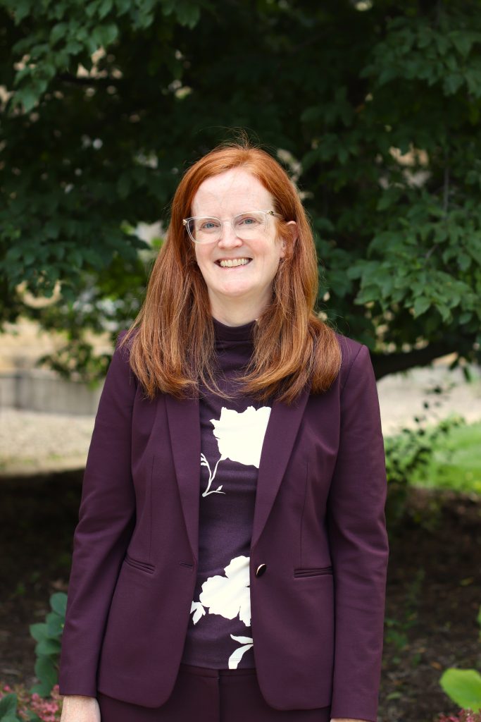 Emily Cauble, a middle-aged woman with fair skin, red hair, and blue eyes.