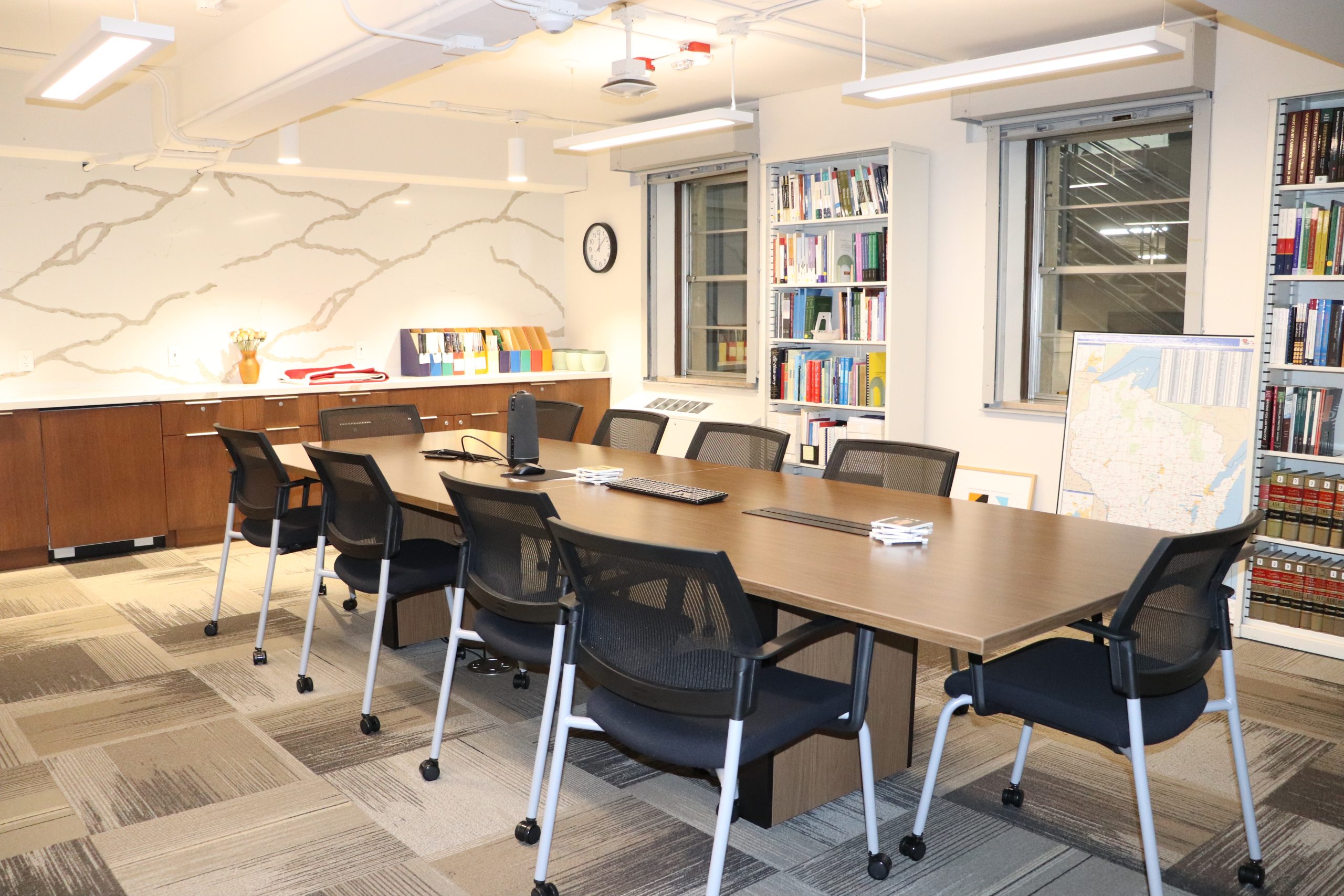 A bright room with warm lights and a long conference table, books on wall shelves, and a large map of Wisconsin.
