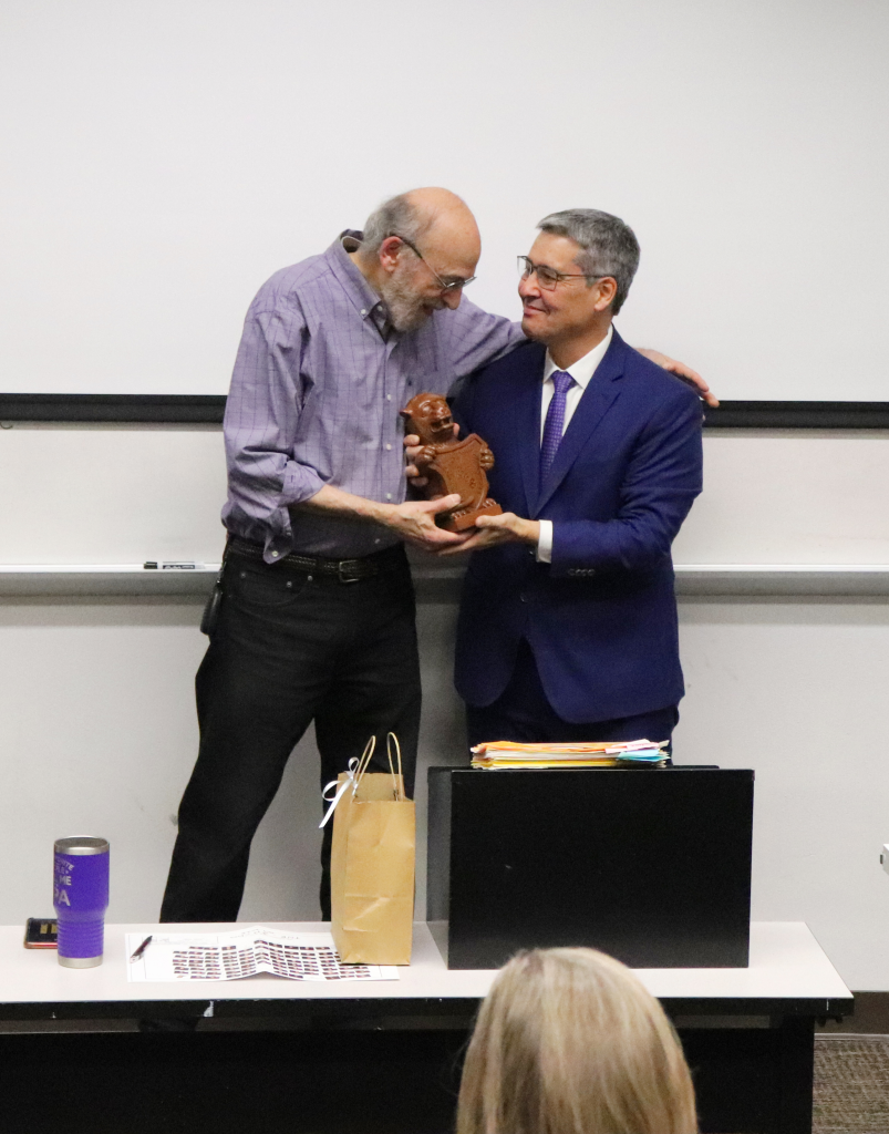an elderly man receives a small statue from a man in a suit