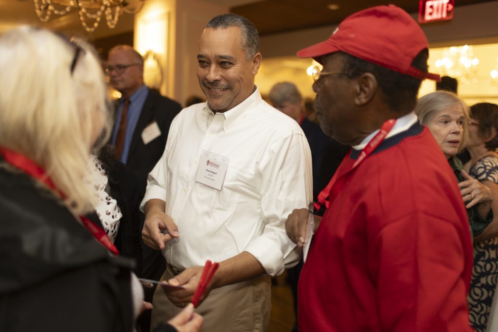 Several black and brown skinned folks stand together while talking.
