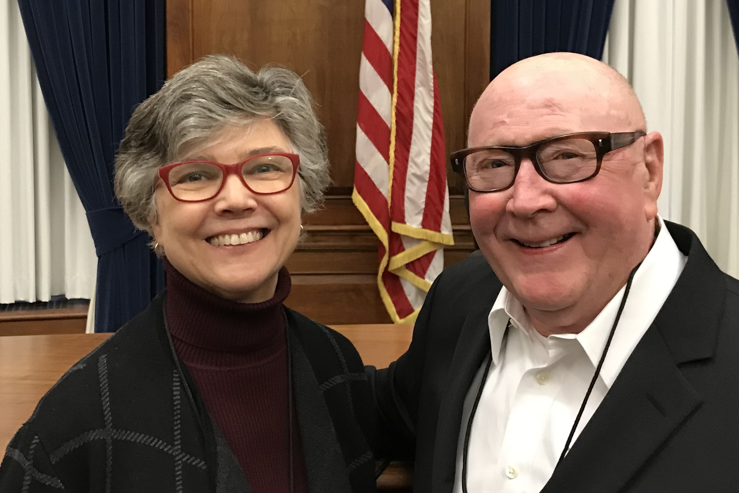 Photo of two seniors together - a gray haired woman with red framed glasses and a bald man with brown frame glasses.