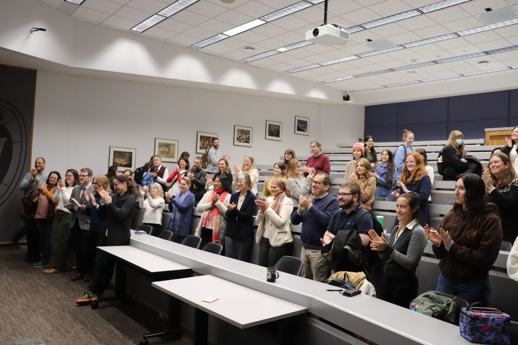 A large number of students are standing and clapping.